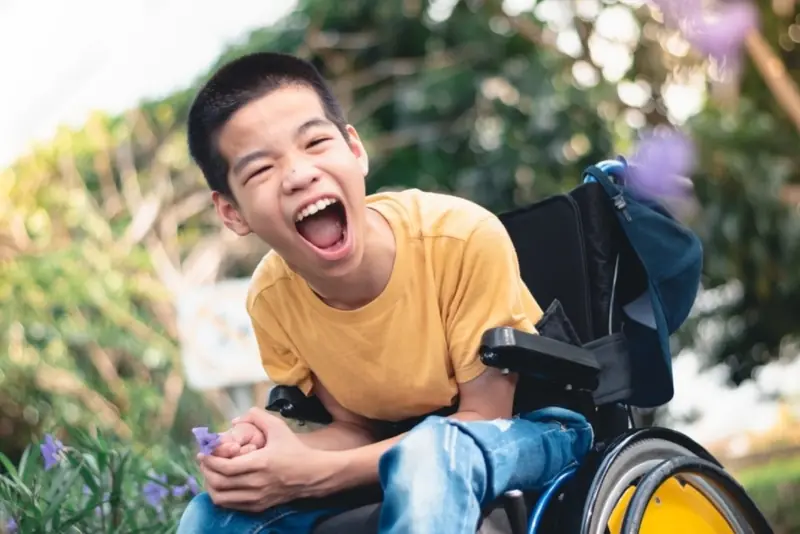 Child in a wheelchair playing outdoors with a carer